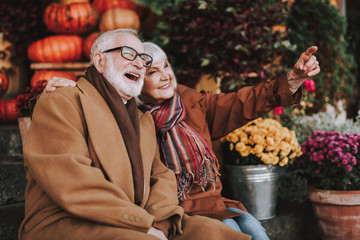 Portrait of cheerful old lady hugging husband and pointing at something while gentleman laughing