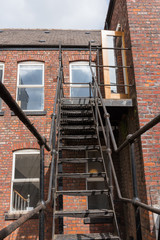 Fototapeta na wymiar urban new york style metal vintage steel fire escape ladder stairs in manchester england. Fire escape route on the side of a building saves lives.