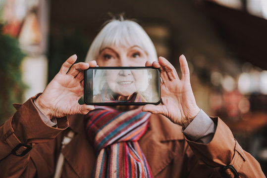 Close up of senior woman holding smartphone and taking photo. Focus on display with picture of lady smile