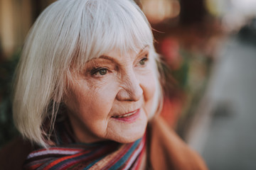 Fototapeta premium Zamyka w górę portreta stara kobieta z siwieje włosy patrzeje daleko od i ono uśmiecha się