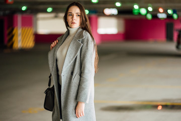 Obraz premium Beautiful young girl in a gray coat and with bag on car parking