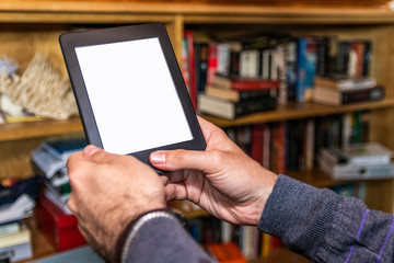 Male hands holding digital reading device in front of bookshelves