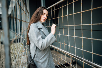 Beautiful young girl in a gray coat behind a fence outdoors