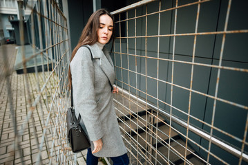 Fototapeta premium Beautiful young girl in a gray coat behind a fence outdoors