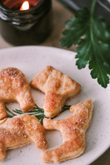 Homemade shaped cookies on a wooden table next to candles and green leaves. The concept of Christmas atmosphere and comfort. Closeup.