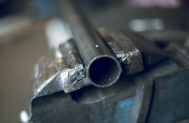 Industrial metal piping, in a vice,  in a cold hard industrial factory setting. Metal iron cut pipes being prepared for scaffolding manufacture. - obrazy, fototapety, plakaty