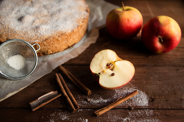 Homemade pie with apples and cinnamon sticks on wooden background.