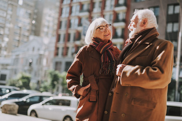 Portrait of stylish bearded gentleman and his lovely wife standing on the street. They wearing coats and scarfs