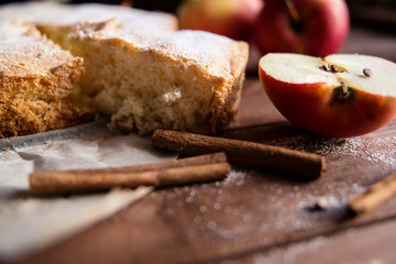 Homemade pie with apples and cinnamon sticks on wooden background.