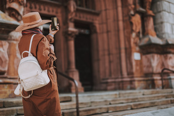 Back view portrait of senior lady with backpack making selfie while standing on the street