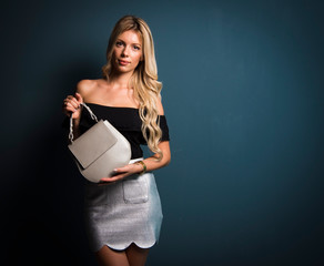 Blonde woman holding little purse on dark gray background