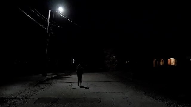 An unidentified person standing in the dark shadows under a city streetlight that&sbquo;&Auml;&ocirc;s short-circuited and is now ominously flashing in the middle of the night.