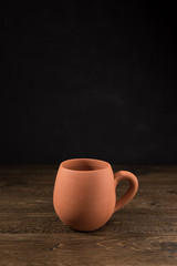 Empty unpainted clay cup on wooden table with black cement texture background