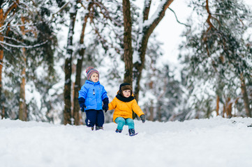 Fototapeta na wymiar Two children going move down hill against snow-covered forest. Funny children's winter games