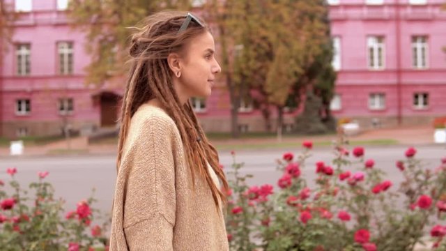portrait young woman with dreadlocks walking along the road on the background red building