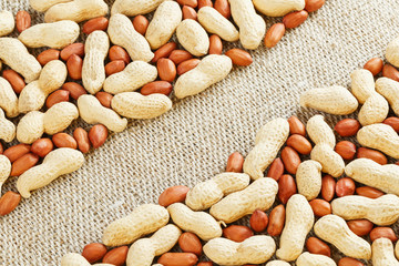 Roasted peanuts in a shell and peeled on a brown fabric background.