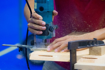 Carpenter working with electric planer on wooden plank in workshop