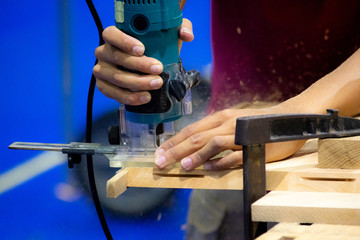 Carpenter working with electric planer on wooden plank in workshop