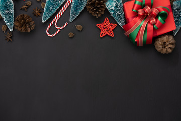 Table top view of Merry Christmas decorations & Happy new year ornaments concept.Flat lay essential objects the fir tree & gift box on modern rustic black wood background at home studio office desk.