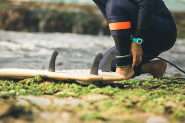 woman surfer tying leg leash with surfboard on seaside reef