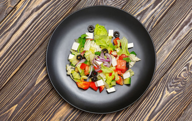 Salad in a plate on wooden background, top view