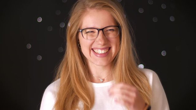 Awesome laughing caucasian female is standing relaxed and showing happiness and wearing glasses on dark background alone, moving, casual style