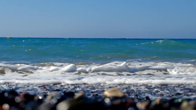 A sunny summer day at the beach, clear and clean blue water, white foam, brown and black shinny rocks in paphos cyprus