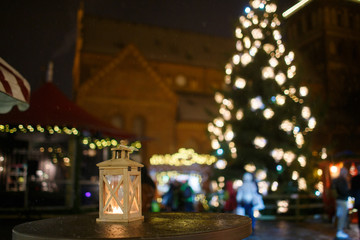 a lantern with a candle on the background of a city fair and a Christmas tree with lights