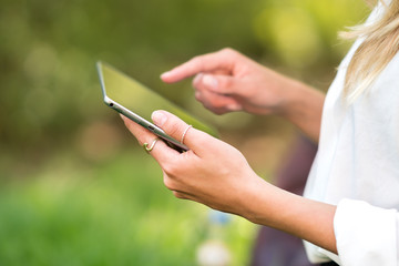 Hands of young woman using tablet outdoors in nature