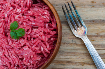 Bowl of raw minced beef meat, metal fork on wooden table background