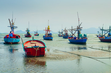 Small fishing boats anchor at beach in cloudy sunset sky.