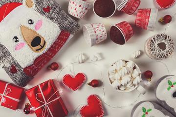 Christmas presents. Knitted sweater, slippers, gift boxes, chocolate muffins and hot chocolate with marshmallow laid on a white wooden table background. Flat lay. Top view. Toned