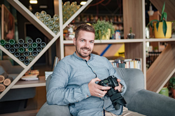 Portrait of a young photographer holding camera while sitting indoors.
