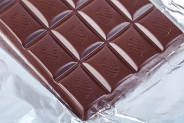 Dark chocolate bar in opened silver foil. Sweet food