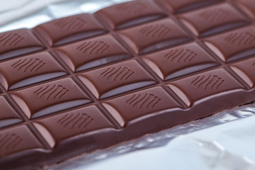 Dark chocolate bar in opened silver foil. Sweet food