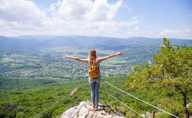 Fototapeta premium Girl with a yellow backpack looking at a beautiful view from the mountain