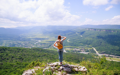 Girl with a yellow backpack looking at a beautiful view from the mountain