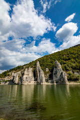 Fototapeta na wymiar Autumn landscape at the Chudnite Skali natural phenomenon, a.k.a Wonderful Cliffs, Bulgaria, scenery cloudy sky with white clouds, green water with rocks refection and still green mountain hills