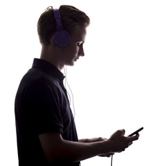 silhouette of a young man listening music in headphones, guy flips through a playlist on smartphone display on a white isolated background