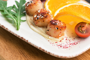Closeup of scallops with sauce and orange, selective focus. Delicacy seafood.