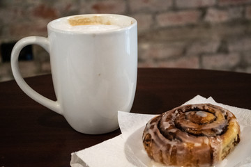 Good Morning! Cappaccino in a white coffee mug next to a sweet cinnamon roll - swirls and frosting. Overhead or closeup shots