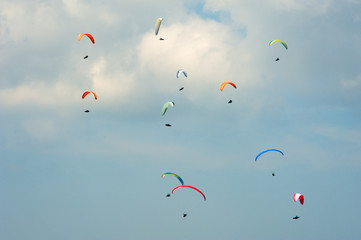 Paragliding in the blue sunny sky. Group of paragliders fly in summer sunny day in the Carpathians. Paragliders against the background of clouds.
