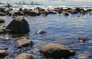 Obraz premium Calm Rockpool with surfer out of water with surfboard and city in the distance