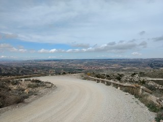 An unpaved country road with a typical rural landscape of Aragon region in Spain, with hills, grass...