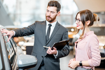 Car salesman helping to a young woman client to make decision showing a new car at the showroom