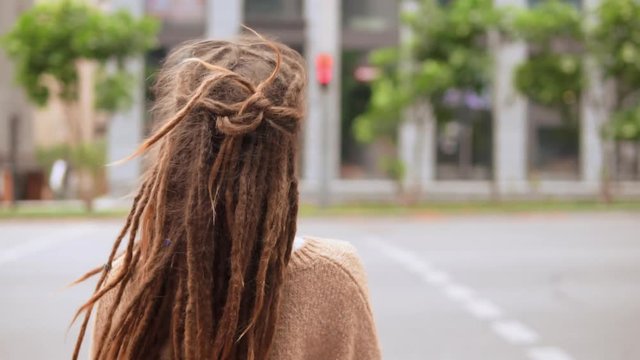 back view close up woman with dreadlocks standing on the street. girl hair fluttering in the wind