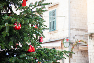 Christmas tree with red balls, bells, white ornaments, street decoration. Background of ancient...