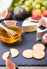 Goat cheese with fresh fruits - figs, grape, honey, cookie cracker on a wooden background, place for text.