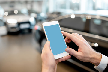 Businessman holding phone with empty screen to copy space in the showroom with cars on the...