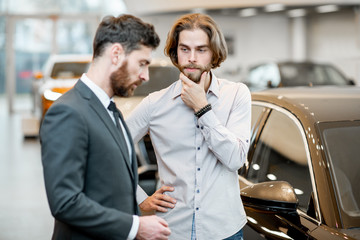 Man client hesitates choosing a car with salesperson in the showroom